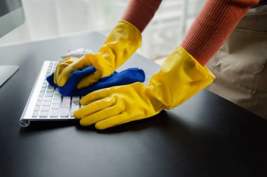 Ofis ekipmanlarını temizleme, klavyeyi havlu ve dezenfektanla silme, temizlik kimyasallarıyla çalışırken lastik eldiven giyme, temizlik fikri..