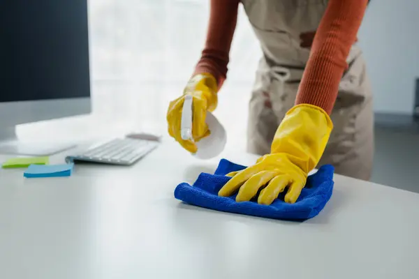 Cleaning desk surface in office with sanitizer spray, wear gloves and wipe the table with a towel, the housekeeper is cleaning the work desk for hygiene because of the Covid-19, cleaning idea.
