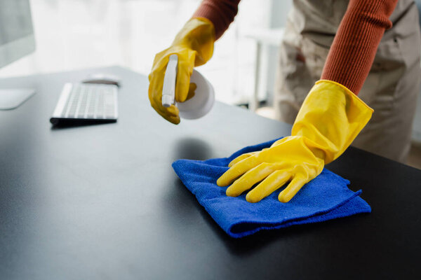 Уборка поверхности рабочего стола в офисе с помощью аэрозоля, ношение перчаток и протирание стола инструментом, уборщица убирает рабочий стол для истерики из-за идеи уборки "Ковид-19".