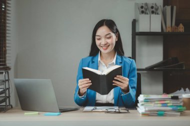 İş kadını ofiste oturuyor ve çalışıyor. Çalışan bilgisayarda bilgi arıyor. Kağıda çeşitli bilgiler kaydediyor..