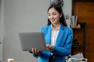 İş kadını ofiste oturuyor ve çalışıyor. Çalışan bilgisayarda bilgi arıyor. Kağıda çeşitli bilgiler kaydediyor..