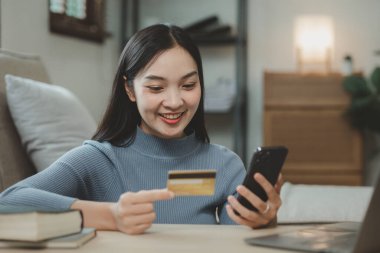 Oturma odasındaki kanepede online alışveriş yapmak, izin günlerinde internet üzerinden ödeme yapmak için kredi kartı kullanmak, hizmet parasını ödemek için kredi kartı bilgilerini girmek için dizüstü bilgisayar kullanmak..