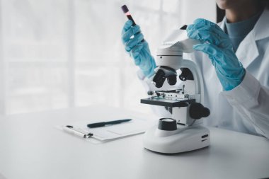 Bir kimyager test tüpündeki kandaki kimyasalları araştırmak için mikroskop kullanıyor bilimsel bir deney laboratuvar, laboratuvar fikri içinde biyolojik cevaplar arıyor..
