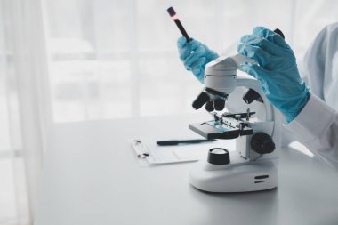 Bir kimyager test tüpündeki kandaki kimyasalları araştırmak için mikroskop kullanıyor bilimsel bir deney laboratuvar, laboratuvar fikri içinde biyolojik cevaplar arıyor..