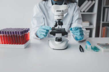 Bir kimyager test tüpündeki kandaki kimyasalları araştırmak için mikroskop kullanıyor bilimsel bir deney laboratuvar, laboratuvar fikri içinde biyolojik cevaplar arıyor..
