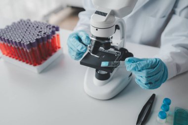 Bir kimyager test tüpündeki kandaki kimyasalları araştırmak için mikroskop kullanıyor bilimsel bir deney laboratuvar, laboratuvar fikri içinde biyolojik cevaplar arıyor..