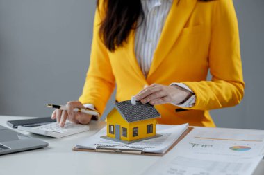 Bir emlakçı ofisinde oturur, satıcı müşterinin almak üzere olduğu evi sunar, komisyoncu alıcının aylık taksitlerini hesaplar..