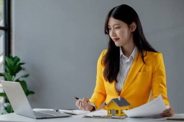 Bir emlakçı ofisinde oturur, satıcı müşterinin almak üzere olduğu evi sunar, komisyoncu alıcının aylık taksitlerini hesaplar..