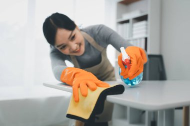 Asyalı kadın temizlikçi, temizlik spreyiyle masaları temizliyor. Temizlikçi, temizlik için çalışma masasını temizliyor..