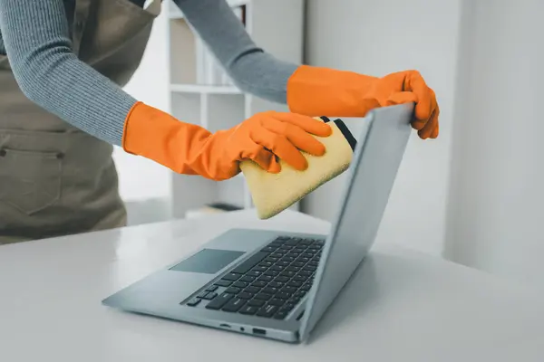 Cleaning staff wiping down office equipment, Clean the notebook with a rag, Janitor cleaning the office, Wear rubber gloves and an apron and work with a happy smile,