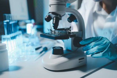 Steril giyim ve güvenlik gözlüklü genç bilim adamları bir tıp laboratuarında mikroskop kullanarak araştırma yürüterek ciddi bir konsantre kadın mikrobiyolog olarak masada oturuyorlar..