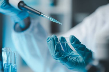 Steril giyim ve güvenlik gözlüklü genç bilim adamları bir tıp laboratuarında mikroskop kullanarak araştırma yürüterek ciddi bir konsantre kadın mikrobiyolog olarak masada oturuyorlar..