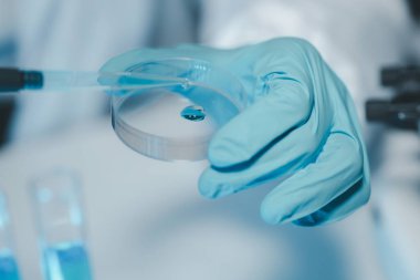 Steril giyim ve güvenlik gözlüklü genç bilim adamları bir tıp laboratuarında mikroskop kullanarak araştırma yürüterek ciddi bir konsantre kadın mikrobiyolog olarak masada oturuyorlar..