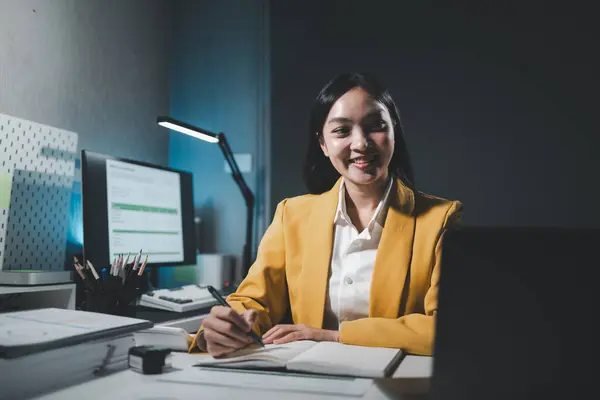 Young Asian businesswoman working overtime in a dark office, Young woman working on the laptop late at night, working overtime in the office to finish the project within the deadline.