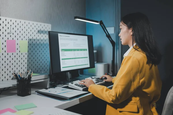 Young Asian businesswoman working overtime in a dark office, Young woman working on the laptop late at night, working overtime in the office to finish the project within the deadline.