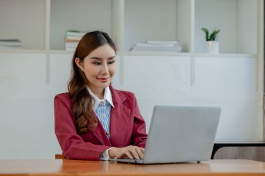 İş kadını ofiste oturuyor ve çalışıyor, Çalışan laptopta bilgi arıyor, çeşitli bilgileri kağıda kaydediyor, çalışanlar oturuyor ve ofiste notlar alıyor.