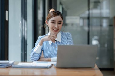 İş kadını ofiste oturuyor ve çalışıyor, Çalışan laptopta bilgi arıyor, çeşitli bilgileri kağıda kaydediyor, çalışanlar oturuyor ve ofiste notlar alıyor.