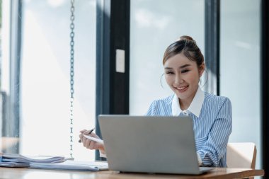 İş kadını ofiste oturuyor ve çalışıyor, Çalışan laptopta bilgi arıyor, çeşitli bilgileri kağıda kaydediyor, çalışanlar oturuyor ve ofiste notlar alıyor.