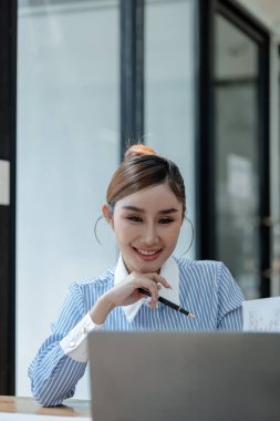 İş kadını ofiste oturuyor ve çalışıyor, Çalışan laptopta bilgi arıyor, çeşitli bilgileri kağıda kaydediyor, çalışanlar oturuyor ve ofiste notlar alıyor.