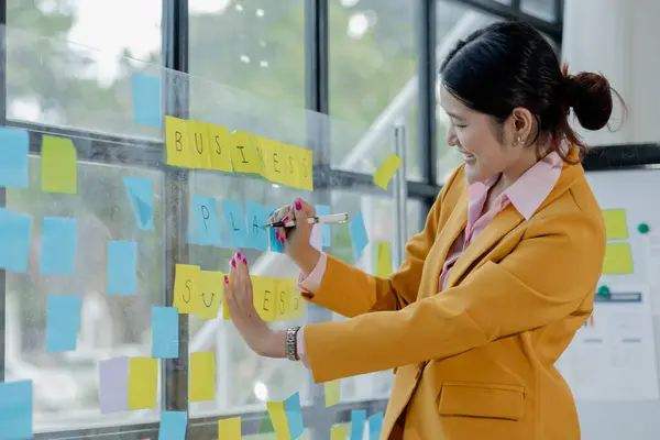 Collaboration is a key to best results. young modern people in smart casual wear planning business strategy while young woman pointing at infographic displayed on the glass wall in the office.