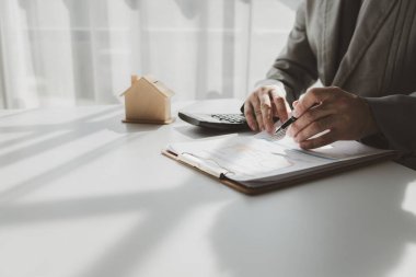 Bir emlakçı ofisinde oturur, satıcı müşterinin almak üzere olduğu evi sunar, komisyoncu alıcının aylık taksitlerini hesaplar..