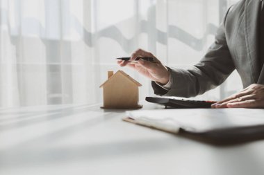 Bir emlakçı ofisinde oturur, satıcı müşterinin almak üzere olduğu evi sunar, komisyoncu alıcının aylık taksitlerini hesaplar..