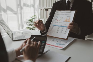 Gelir hesaplamak için birlikte çalışan bir grup işadamı, finansal rakamları gözden geçiriyorlar, finansal belgeleri çıkarıyorlar ve hesap makinesiyle kontrol ediyorlar.,