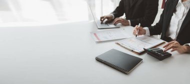 Gelir hesaplamak için birlikte çalışan bir grup işadamı, finansal rakamları gözden geçiriyorlar, finansal belgeleri çıkarıyorlar ve hesap makinesiyle kontrol ediyorlar.,