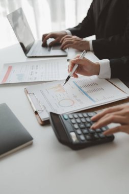 Gelir hesaplamak için birlikte çalışan bir grup işadamı, finansal rakamları gözden geçiriyorlar, finansal belgeleri çıkarıyorlar ve hesap makinesiyle kontrol ediyorlar.,