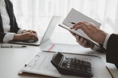 Çalışanlar ofiste oturur ve notlar alır, bir iş adamı bir dizüstü bilgisayardan bilgi arar ve bunu bir deftere yazar, ofisteki ekiple iş kurma işini tartışır.,