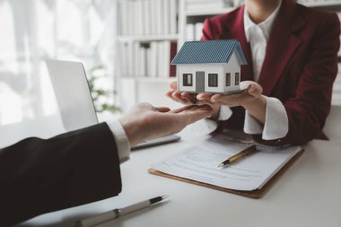 Komisyoncu alıcının aylık taksit ödemelerini hesaplıyor, emlak komisyoncusu müşteriye sigorta sözleşmesi imzalama, ev modeli alıp satma kararını sunuyor ve danışmanlık yapıyor.,
