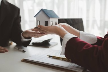 Komisyoncu alıcının aylık taksit ödemelerini hesaplıyor, emlak komisyoncusu müşteriye sigorta sözleşmesi imzalama, ev modeli alıp satma kararını sunuyor ve danışmanlık yapıyor.,
