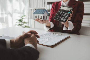 Bir emlakçı ofisinde oturur, satıcı müşterinin almak üzere olduğu evi sunar, komisyoncu alıcının aylık taksitlerini hesaplar..