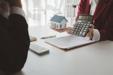 Bir emlakçı ofisinde oturur, satıcı müşterinin almak üzere olduğu evi sunar, komisyoncu alıcının aylık taksitlerini hesaplar..