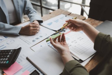 Finansal belgeleri al ve hesap makinesiyle kontrol et, şirket içindeki harcamalar için finansman planlıyorlar, toplantıya gönderilen rapora göre rakamları hesaplıyorlar., 