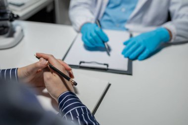 Konuşmada doktor ve hasta, erkek doktor danışmanlık yapıyor. Konsültasyonda hasta muayene ediyor. Profesyonel doktor beyaz önlük giyiyor ve randevuda olgun bir kadınla konuşuyor.,