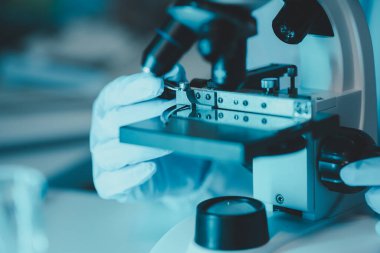 Laboratuvarda mikroskop analizi yapan üniformalı kadın sıhhiyeci, metal mercekli mikroskobun yakın plan çekimini yapan bir bilim adamı, kimyasal bileşimi analiz etmek için mikroskop kullanıyor., 
