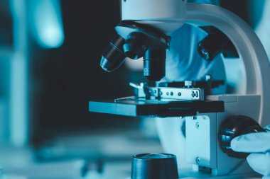 Laboratuvarda mikroskop analizi yapan üniformalı kadın sıhhiyeci, metal mercekli mikroskobun yakın plan çekimini yapan bir bilim adamı, kimyasal bileşimi analiz etmek için mikroskop kullanıyor., 