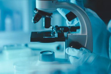 Laboratuvarda mikroskop analizi yapan üniformalı kadın sıhhiyeci, metal mercekli mikroskobun yakın plan çekimini yapan bir bilim adamı, kimyasal bileşimi analiz etmek için mikroskop kullanıyor., 