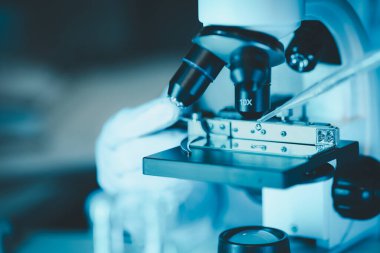 Laboratuvarda mikroskop analizi yapan üniformalı kadın sıhhiyeci, metal mercekli mikroskobun yakın plan çekimini yapan bir bilim adamı, kimyasal bileşimi analiz etmek için mikroskop kullanıyor., 