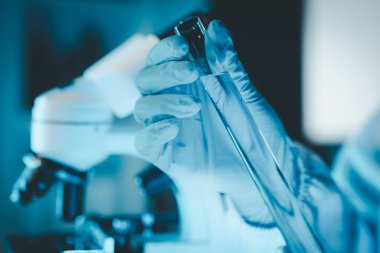 Araştırma laboratuarında teknisyen tüpü testi, kimyagerin elinde laboratuarda analiz makineleri bulunan bir raftan solüsyon örneği tüpü, pipetten tüpe sıvı damlatıyor..