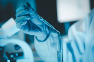 Araştırma laboratuarında teknisyen tüpü testi, kimyagerin elinde laboratuarda analiz makineleri bulunan bir raftan solüsyon örneği tüpü, pipetten tüpe sıvı damlatıyor..