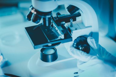 Laboratuvarda mikroskop analizi yapan üniformalı kadın sıhhiyeci, metal mercekli mikroskobun yakın plan çekimini yapan bir bilim adamı, kimyasal bileşimi analiz etmek için mikroskop kullanıyor., 