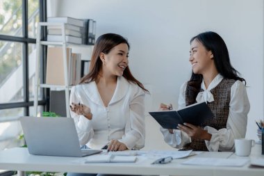 Ofiste dizüstü bilgisayar kullanan neşeli iş adamları, modern bir çalışma alanında birlikte çalışırken gülümseyen genç girişimciler, bir masada birlikte oturan iki genç iş adamı..