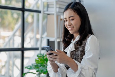 Bir girişimci, bir şirket müşterisiyle telefonda konuşuyor, ofiste güzel bir kadın, mutlu, iş kadını akıllı telefondan e-postaları kontrol ediyor, yönetici cep telefonu kullanıyor., 