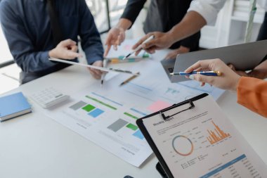 Çalışanlardan oluşan bir grup, yaklaşan bir etkinliğin detaylarını, toplantı durumunu yakından inceliyor. İş adamları ve kadınlar, şeffaf bir konferans odasında gergin bir toplantı yapıyorlar..