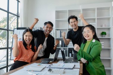 Neşeli iş adamları, serbest girişimciler, çalışmalarını bitirdikten sonra masasında otururken zaferle gülümseyen ve sevinen, heyecanlı, mutlu bir şirket üyesi, aşırı motive olmuş,.