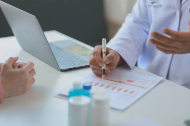 Erkek pratisyen doktor hastaya, doktora ve hastaya güvence veriyor, Asyalı erkek doktor hastaya danışmanlık yapıyor, profesyonel doktor beyaz önlüklü, olgun bir kadınla konuşuyor.