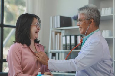 Genç bir Asyalı kadın hasta, bir tıp uzmanı tarafından muayene ediliyor, onurlu orta yaşlı bir erkek doktor, bir tedavi planlamak için bir hastanın vücuduna teşhis koyuyor..