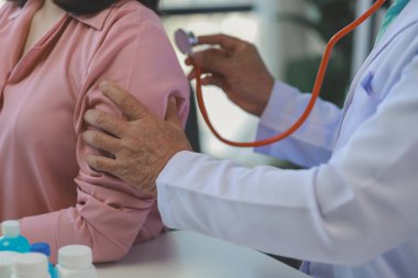 Genç bir Asyalı kadın hasta, bir tıp uzmanı tarafından muayene ediliyor, onurlu orta yaşlı bir erkek doktor, bir tedavi planlamak için bir hastanın vücuduna teşhis koyuyor..